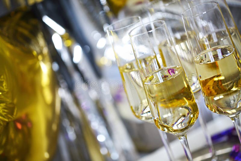 Close up of shiny glasses of champagne over black, white, golden and silver balloons