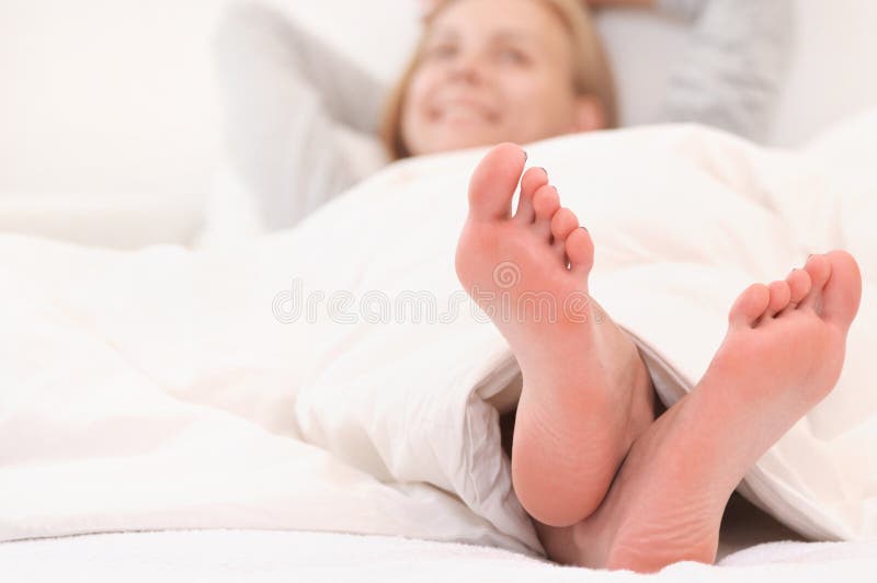 Close up shoot of woman`s feet relaxing in white bed in the morning