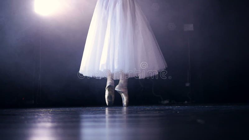 A dark stage behind white dancing ballerinas legs.