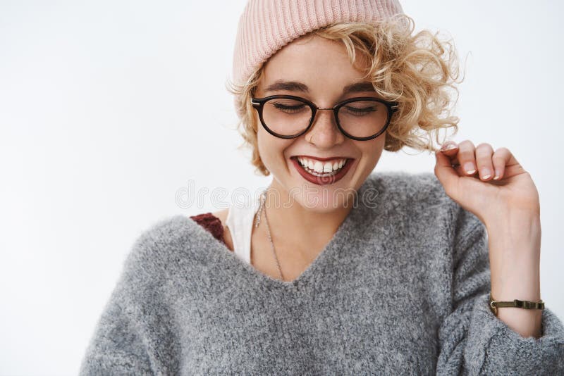 Close-up shot of funny cute and tender joyful woman in glasses beanie and warm winter sweater playing with hair curl