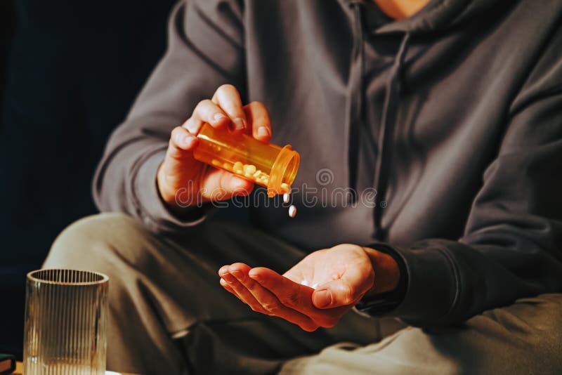 Man pouring tablets from orange plastic bottle into his hand. Medication, addiction, pain concept