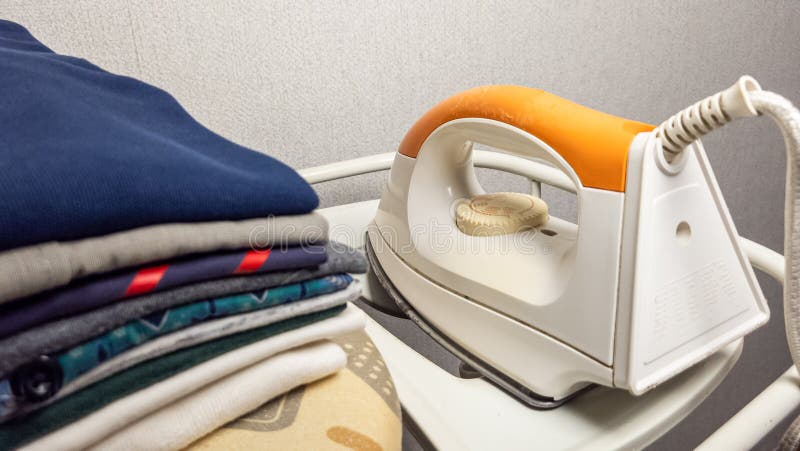 Stack of Folded Clothes and a White and Orange Iron Ready for Use stock photography