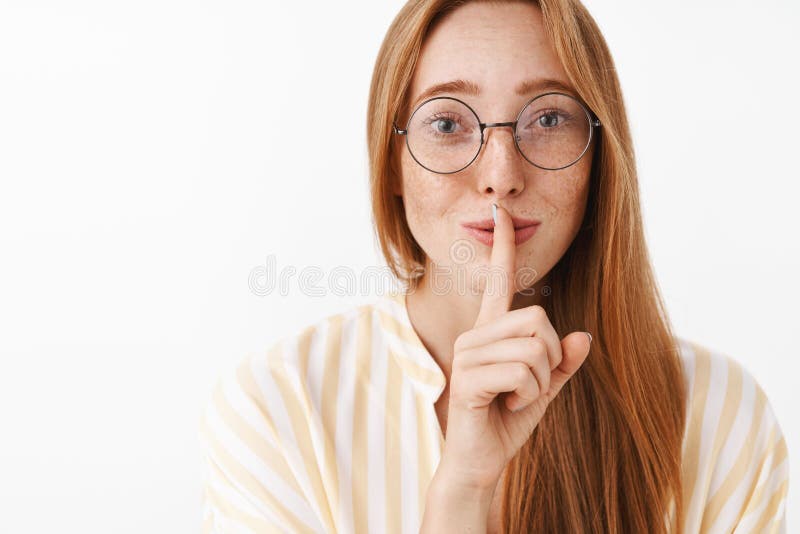 Close-up shot of tender and feminine cute redhead female in glasses with freckles showing shh sign making shush sound stock photos Close-up shot of tender and feminine cute redhead female in glasses with freckles showing shh sign making shush sound stock photos