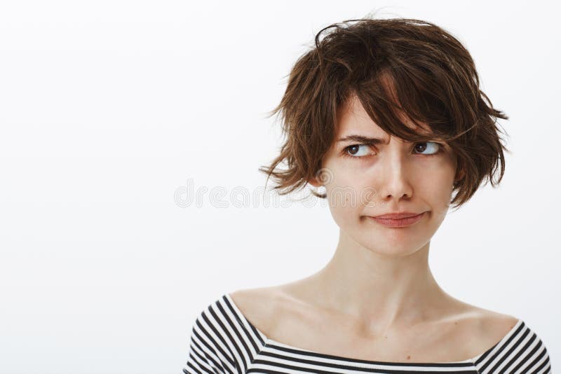 Close-up shot of unsure intense good-looking girl with stylish short haircut, frowning and pulling smile while frowning