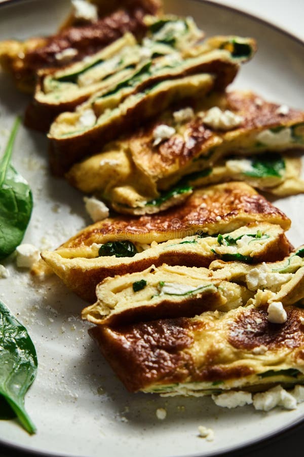Close up of sliced folded omelette stuffed with spinach and feta on the white plate with spinach leaves on back. Healthy royalty free stock photos Close up of sliced folded omelette stuffed with spinach and feta on the white plate with spinach leaves on back. Healthy royalty free stock photos