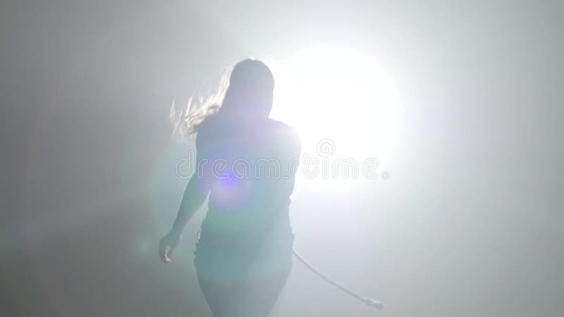 Close-up slow motion. Young girl practicing capoeira in ray of spotlight in studio.