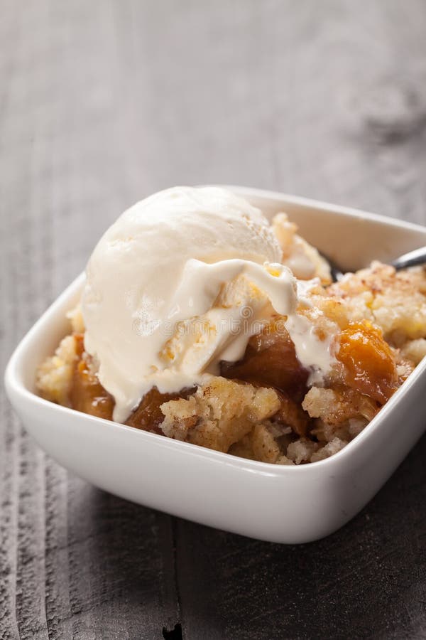 Close up of mall bowl of freshly served peach crisp with scoop of ice cream on top. Close up of mall bowl of freshly served peach crisp with scoop of ice cream on top