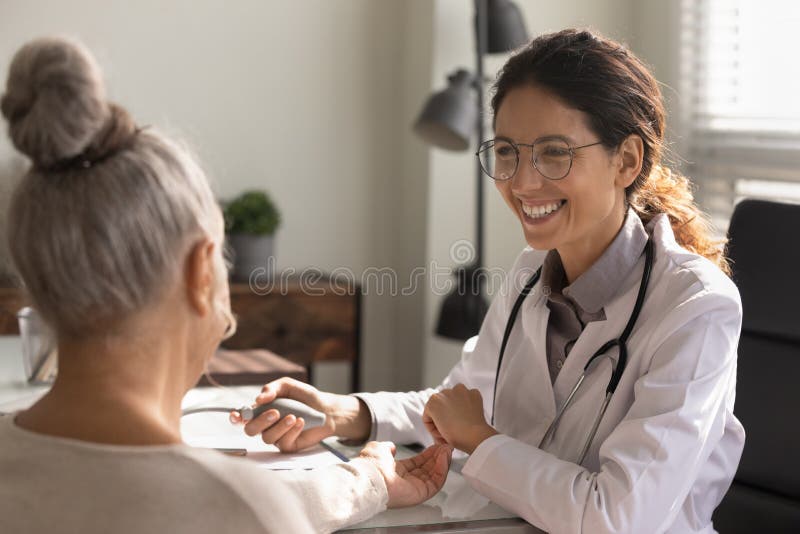 Close up smiling female doctor checking old woman blood pressure. Close up smiling female doctor wearing glasses checking old woman blood pressure at meeting in