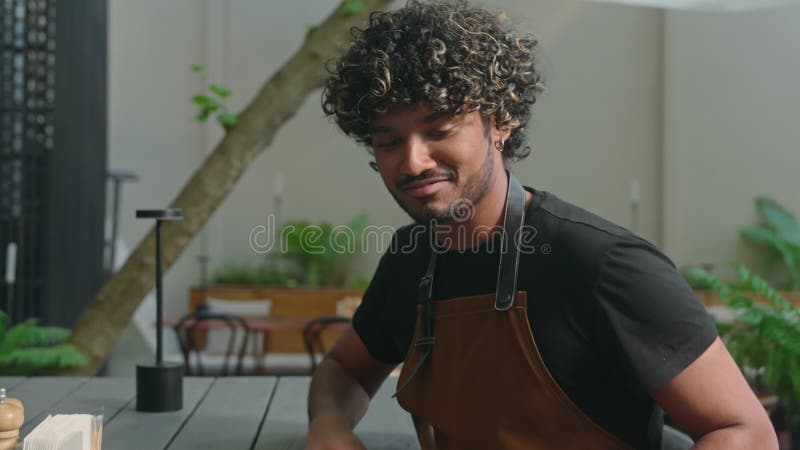 Close up smiling Latino American ethnic man male cafe worker in apron guy waiter cleaner barista wiping table in stock video