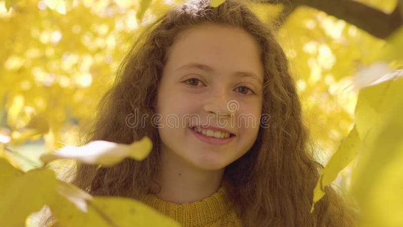 Close-up of a smiling redhead caucasian girl in mustard sweater looking at the camera. Child with long curly hair and