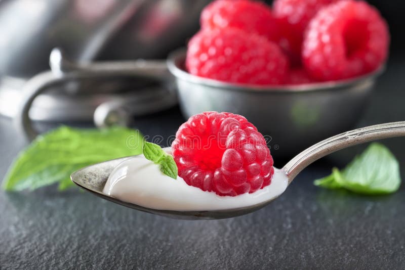 Close-up on a spoon of yougurt with juisy raspberry on top with berries and meant leaves stock photos Close-up on a spoon of yougurt with juisy raspberry on top with berries and meant leaves stock photos