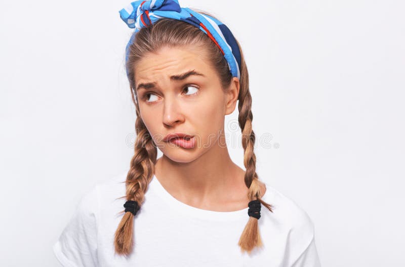 Close-up studio portrait of thoughtful blonde beautiful young woman wears wghite t-shirt, blue headband and braids hairstyle