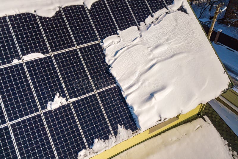 Close up surface of a house roof covered with solar panels in winter with snow on top. Energy efficiency and maintenance concept