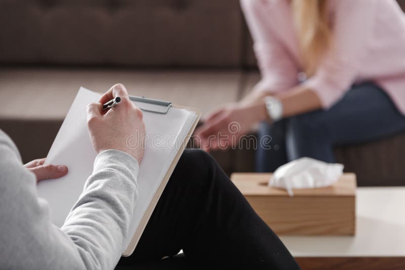 Close-up of therapist hand writing notes during a counseling session with a single woman sitting on a couch in the blurred