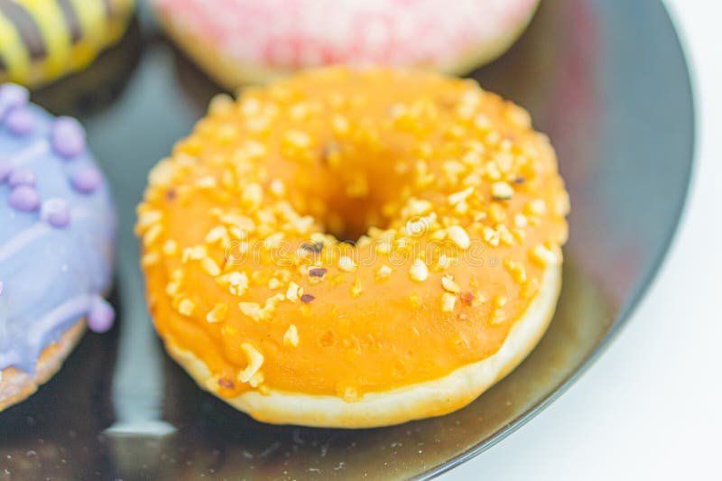 Close-up of three donuts on a reflective surface, with the central one glossy orange and nutty, and others partially stock photography