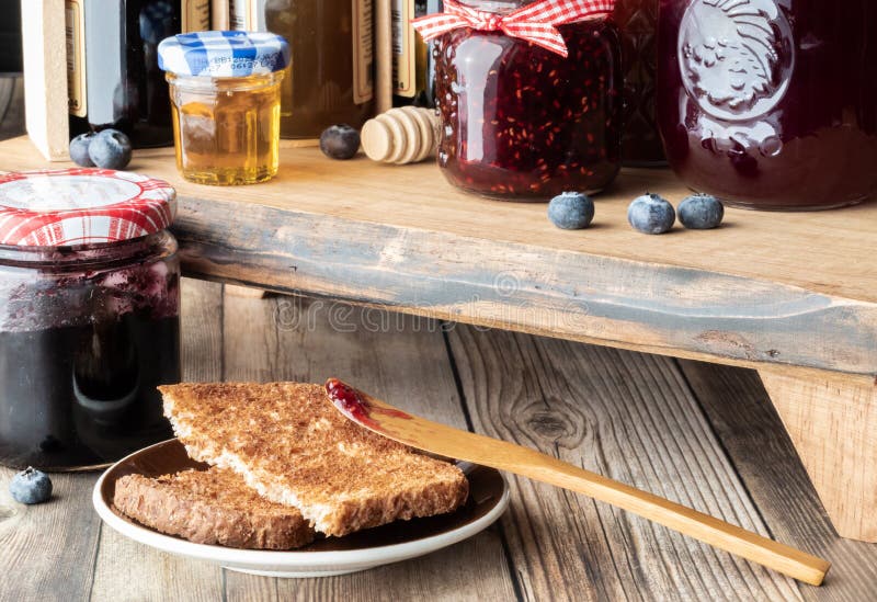 Close up of pieces of toast with raspberry jam on a wooden spoon surrounded by jars of jam and honey. Various sweet preserves stock images, royalty-free photos and pictures