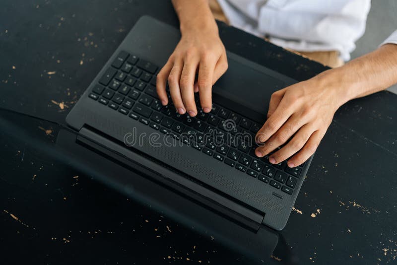 Close-up top view of unrecognizable young man typing texting on modern laptop keyboard, male employee sitting at black desk working on computer, consult client or studying online, technology concept.