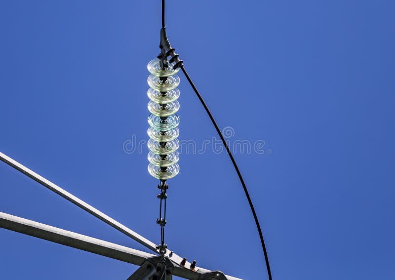 Close up of a transparent turquoise high voltage insulator or isolator in sunlight on electric tower on blue sky background.