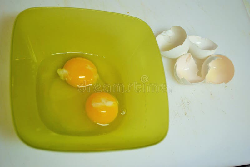 Close Up of Two Raw Eggs in a Green Plastic Bowl and Eggshells Stock