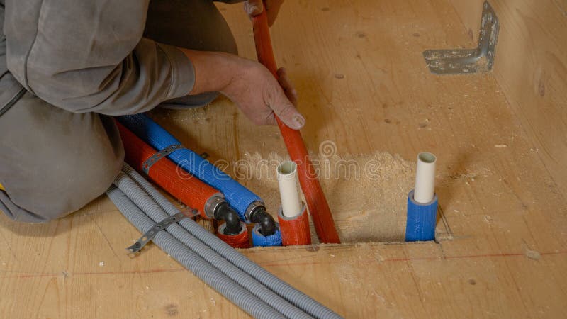 CLOSE UP: Unrecognizable plumber pushes hoses down a hole in the hardwood floor. stock images