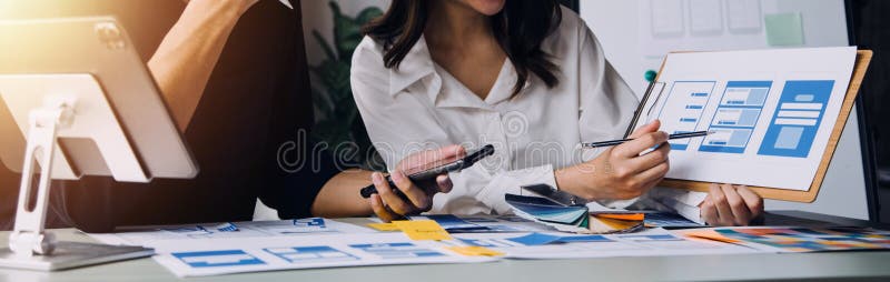 Close up ux developer and ui designer brainstorming about mobile app interface wireframe design on table with customer breif and stock images
