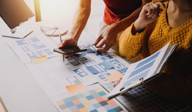 Close up ux developer and ui designer brainstorming about mobile app interface wireframe design on table with customer breif and stock photography