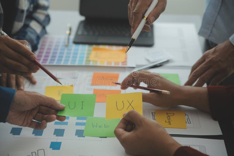 Close up ux developer and ui designer brainstorming about mobile app interface wireframe design on table with customer breif and stock images