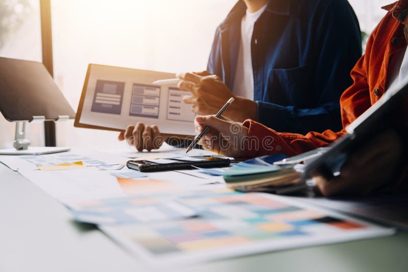 Close up ux developer and ui designer brainstorming about mobile app interface wireframe design on table with customer breif and stock photos