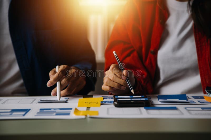 Close up ux developer and ui designer brainstorming about mobile app interface wireframe design on table with customer breif and stock photography