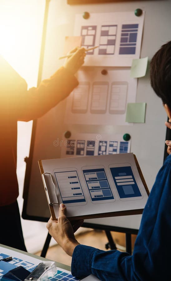 Close up ux developer and ui designer brainstorming about mobile app interface wireframe design on table with customer breif and stock photos