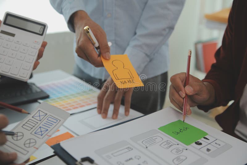 Close up ux developer and ui designer brainstorming about mobile app interface wireframe design on table with customer breif and stock image