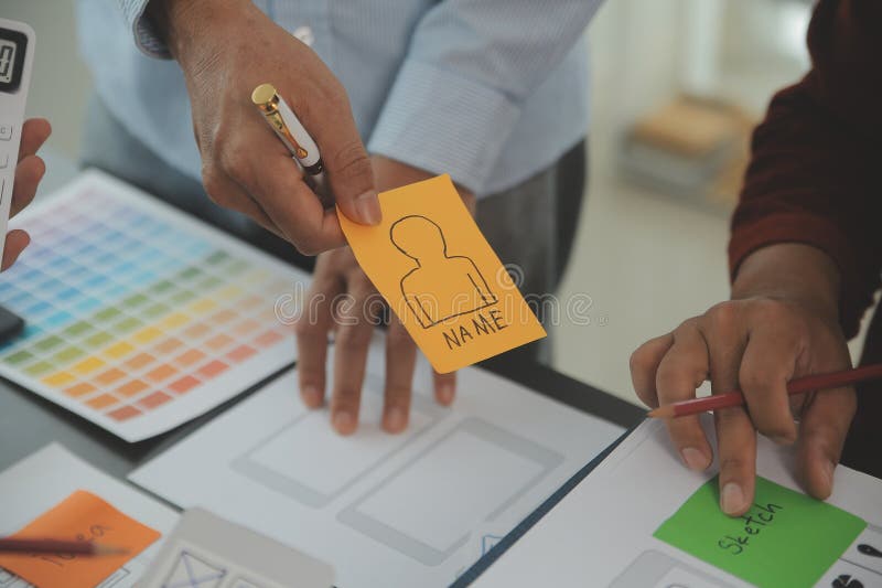 Close up ux developer and ui designer brainstorming about mobile app interface wireframe design on table with customer breif and stock photography