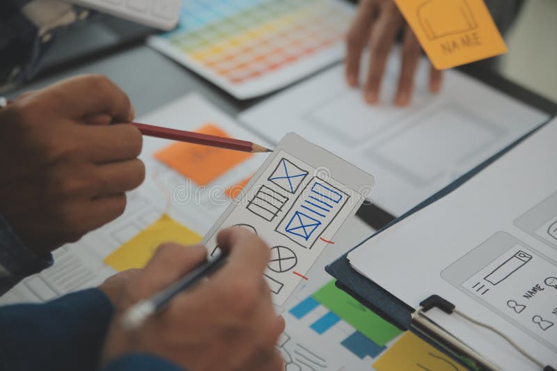 Close up ux developer and ui designer brainstorming about mobile app interface wireframe design on table with customer breif and stock images