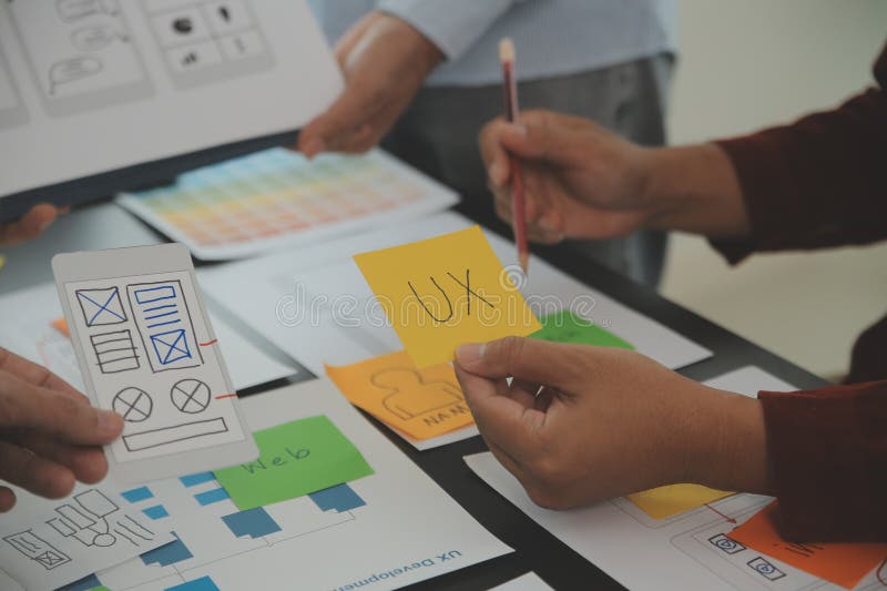 Close up ux developer and ui designer brainstorming about mobile app interface wireframe design on table with customer breif and stock image