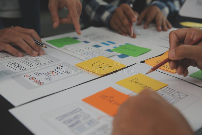Close up ux developer and ui designer brainstorming about mobile app interface wireframe design on table with customer breif and stock images