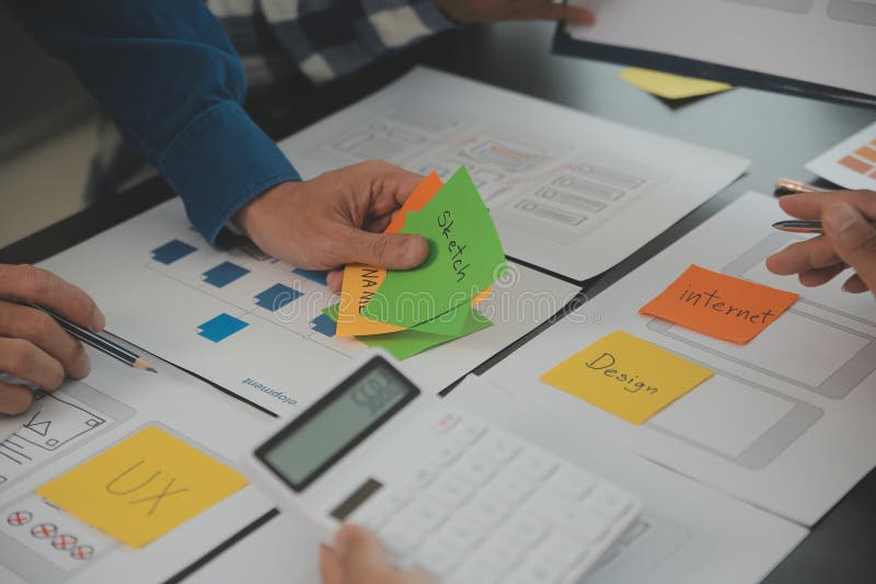 Close up ux developer and ui designer brainstorming about mobile app interface wireframe design on table with customer breif and stock photo
