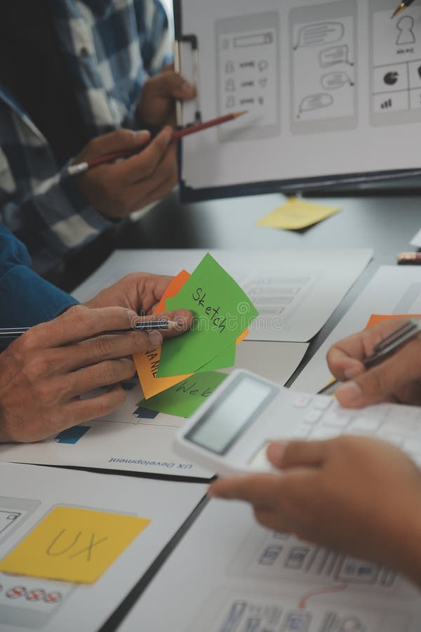Close up ux developer and ui designer brainstorming about mobile app interface wireframe design on table with customer breif and stock photography