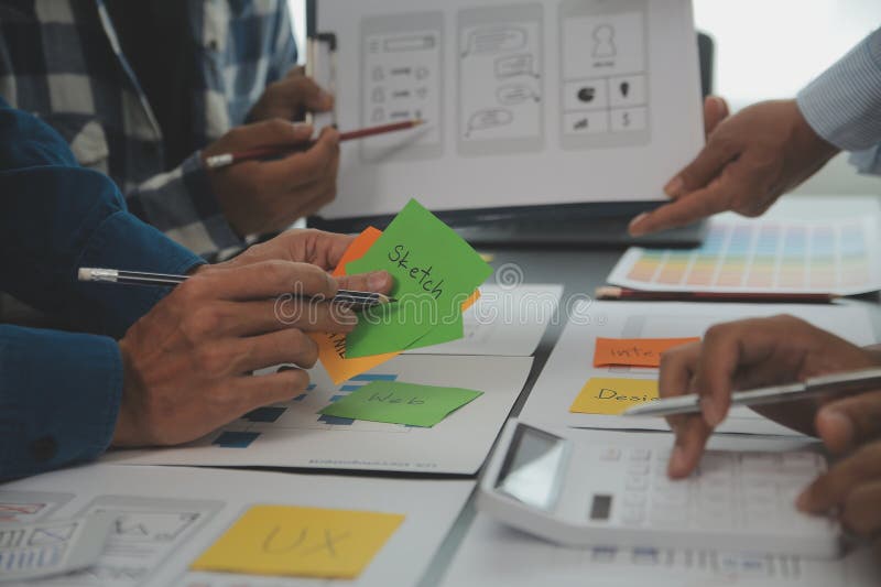 Close up ux developer and ui designer brainstorming about mobile app interface wireframe design on table with customer breif and stock images
