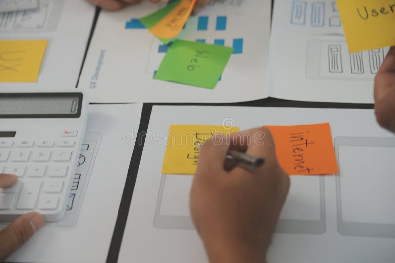 Close up ux developer and ui designer brainstorming about mobile app interface wireframe design on table with customer breif and stock image