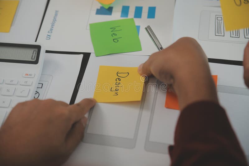 Close up ux developer and ui designer brainstorming about mobile app interface wireframe design on table with customer breif and stock images