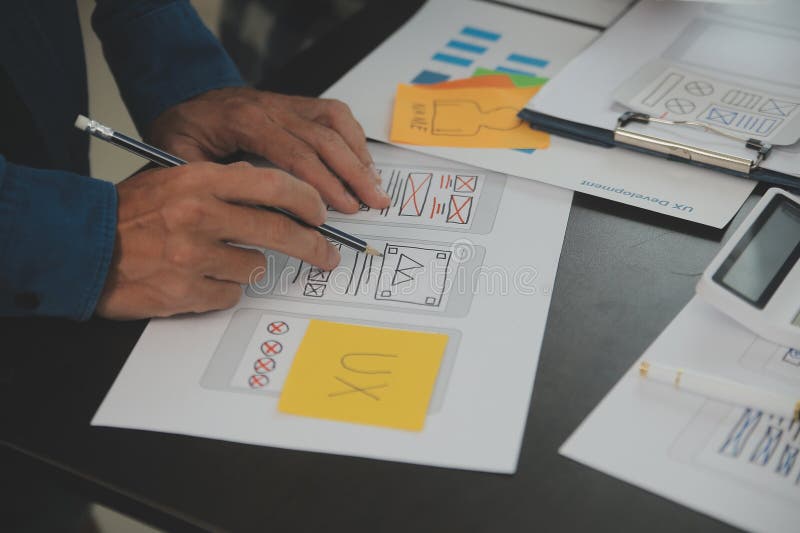Close up ux developer and ui designer brainstorming about mobile app interface wireframe design on table with customer breif and royalty free stock photo