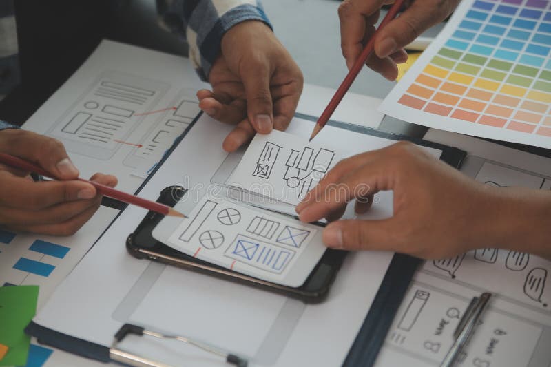 Close up ux developer and ui designer brainstorming about mobile app interface wireframe design on table with customer breif and stock photo