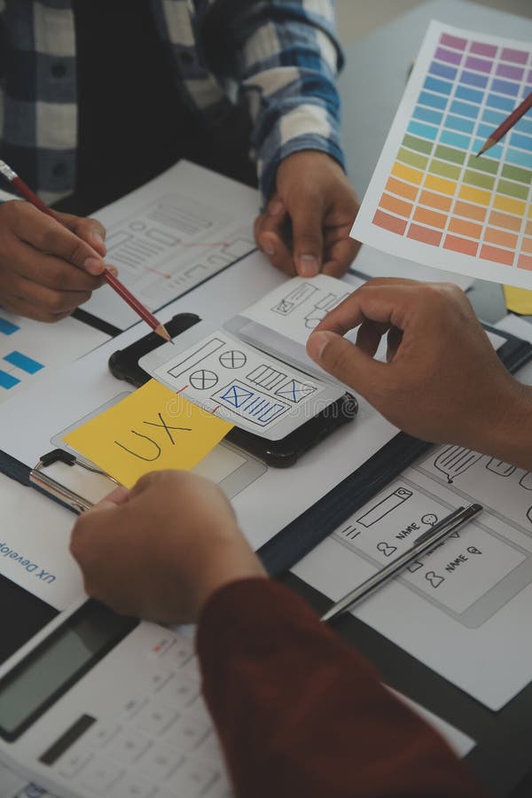 Close up ux developer and ui designer brainstorming about mobile app interface wireframe design on table with customer breif and stock photography