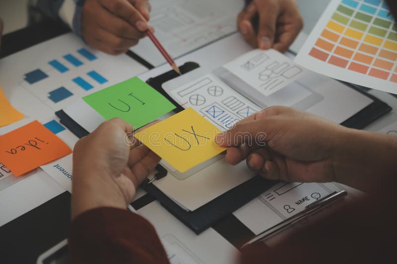 Close up ux developer and ui designer brainstorming about mobile app interface wireframe design on table with customer breif and stock images
