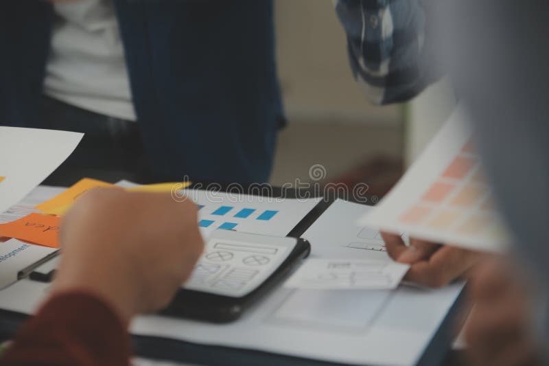 Close up ux developer and ui designer brainstorming about mobile app interface wireframe design on table with customer breif and stock image