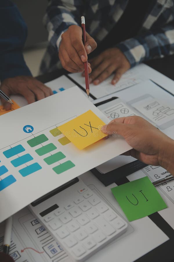 Close up ux developer and ui designer brainstorming about mobile app interface wireframe design on table with customer breif and stock photos