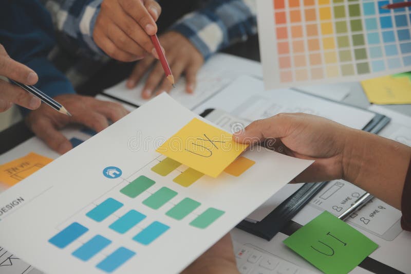 Close up ux developer and ui designer brainstorming about mobile app interface wireframe design on table with customer breif and stock photos
