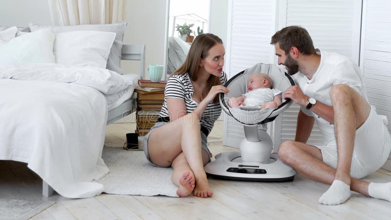 Close-up van gelukkige ouders die op hun kleine babyslaap als schommelende zuigelingsvoorzitter thuis letten in een witte flat E