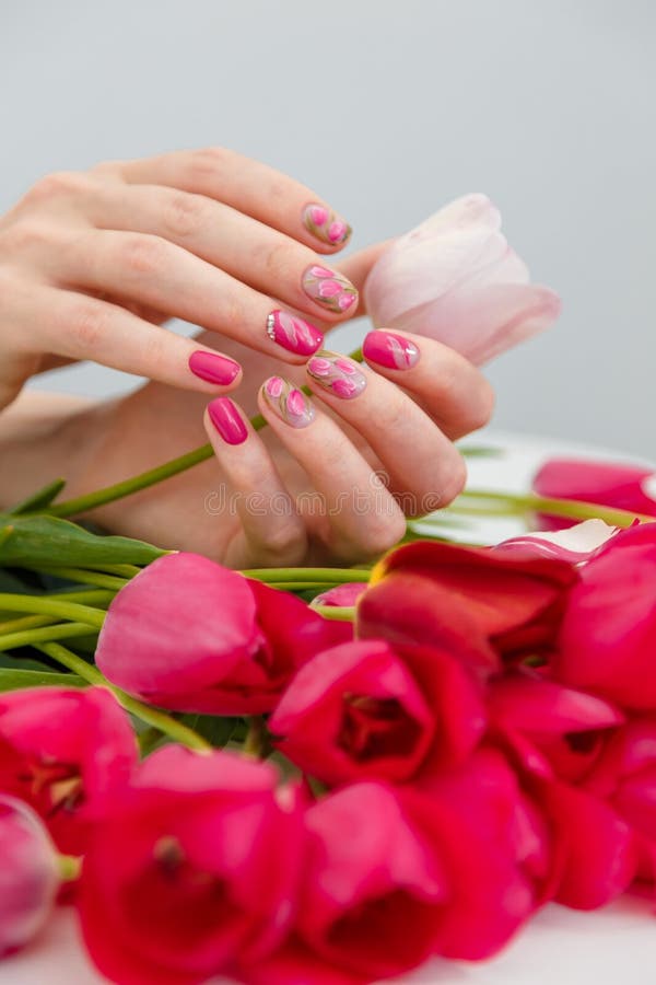 Close up vertical shot of woman hands with spring manicure holding pink tulip on tulips bouquet background. Nail art