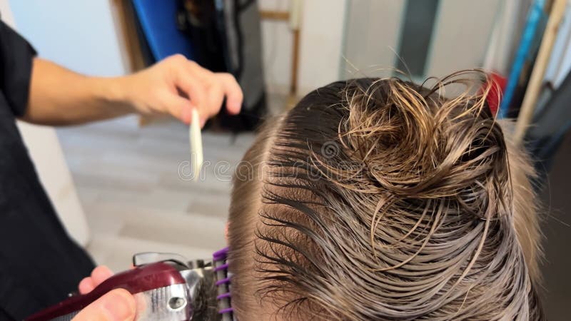 Close-up view of barber trimming trendy 2024 haircut. Process of making hair style at beauty salon. Shaving sides of